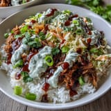 Overhead view of a hearty Pulled Pork Bowl topped with tangy coleslaw, green onions, and a generous drizzle of barbecue sauce.