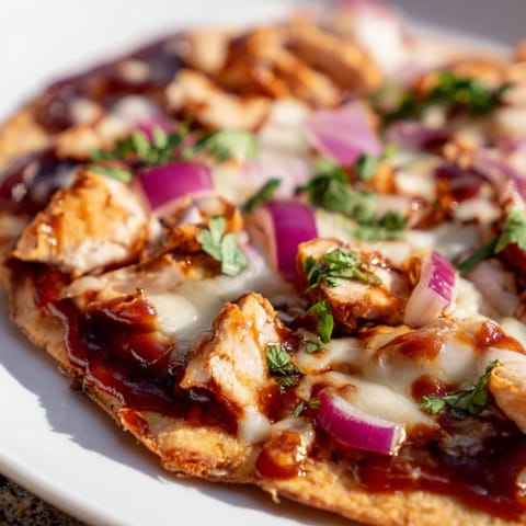 A close-up of golden-brown BBQ Chicken Flatbread, topped with tender grilled chicken, sweet red onions, and melted mozzarella, finished with a fresh cilantro garnish.  