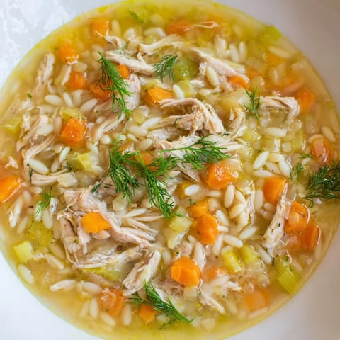 Close-up of Chicken Lemon Orzo Soup with bright lemon zest and chunks of chicken, served hot in a rustic ceramic bowl for a comforting meal.