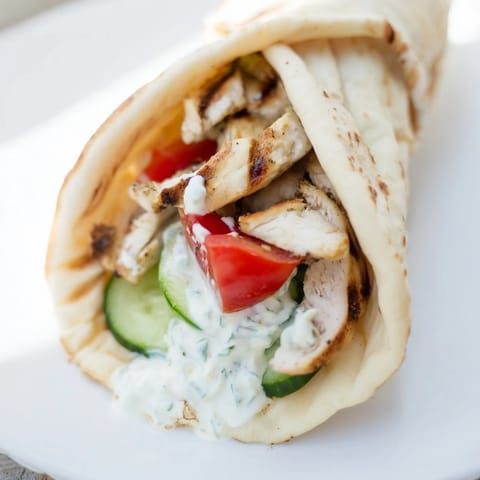 A close-up of a Greek Chicken Wrap reveals juicy grilled chicken strips nestled with cool cucumber and ripe tomato slices.