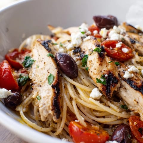Tossing al dente Greek Chicken Spaghetti with Kalamata olives and fresh parsley in a skillet.