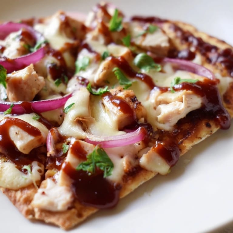 Slice of freshly baked BBQ Chicken Flatbread held over a plate, showcasing gooey mozzarella and tangy BBQ sauce dripping from the edges.  