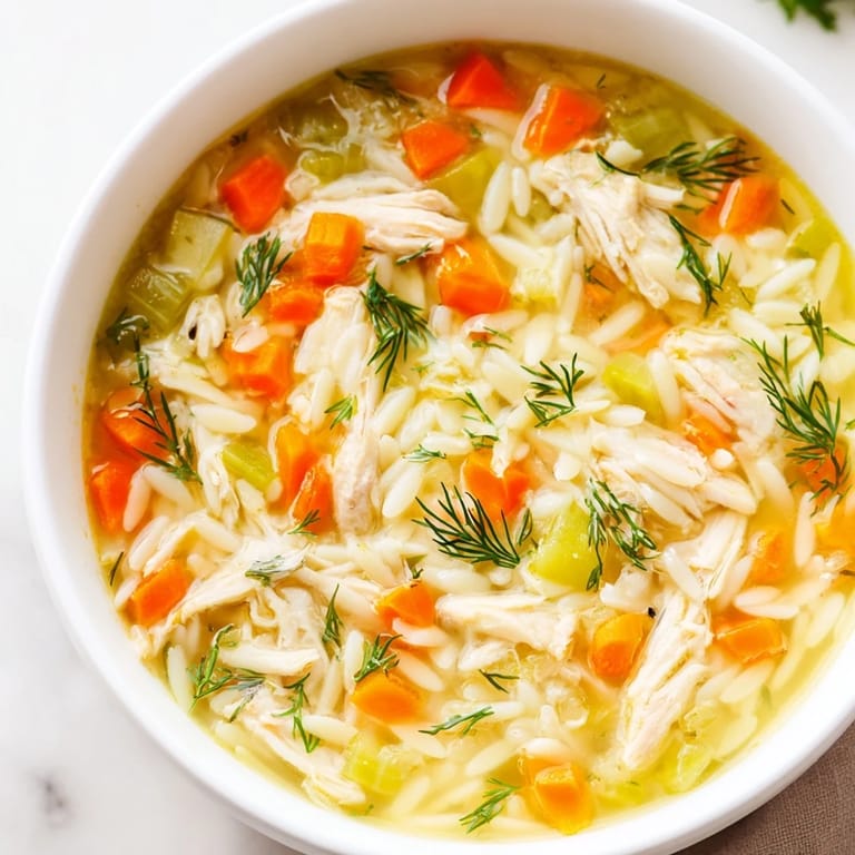 Healthy Chicken Lemon Orzo Soup in a white bowl, featuring colorful carrots and celery, ready to enjoy with a side of crusty bread.