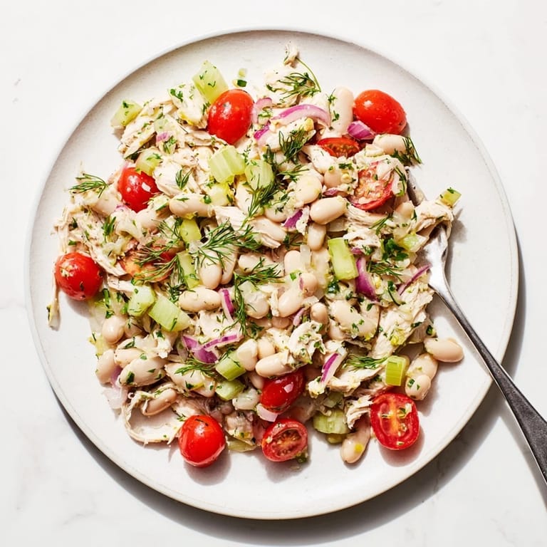A close-up of Lemony White Bean Chicken Salad in a white bowl, garnished with parsley and served alongside crusty bread for a light lunch.