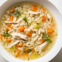 A steaming bowl of homemade Chicken Lemon Orzo Soup garnished with fresh dill, showcasing tender chicken and golden orzo in a clear, aromatic broth.