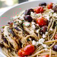 Vibrant Greek Chicken Spaghetti with grilled chicken, cherry tomatoes, and crumbled feta on a white plate.